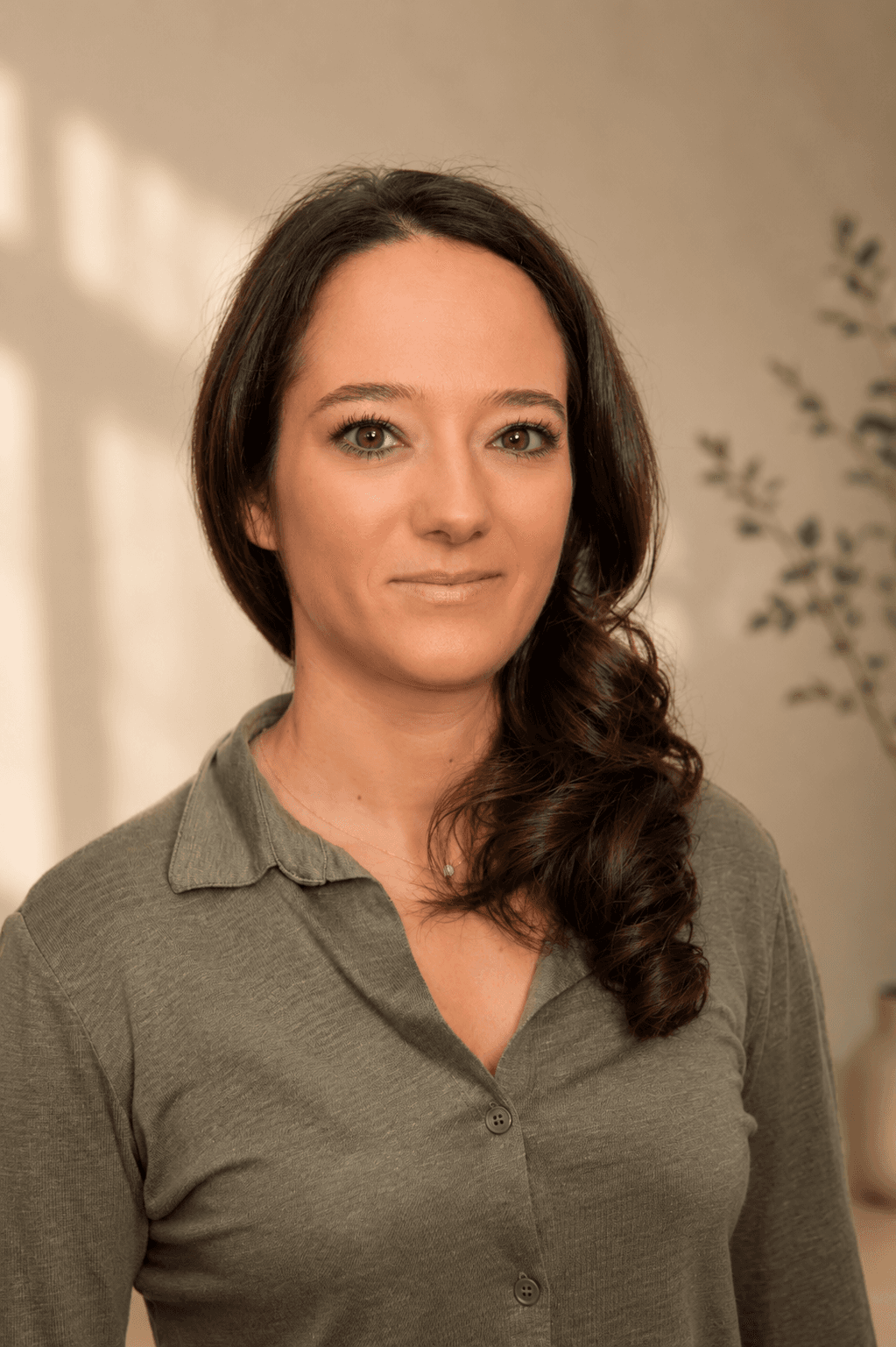 Portrait d'une femme aux cheveux bruns ondulés portant une chemise vert olive boutonnée.