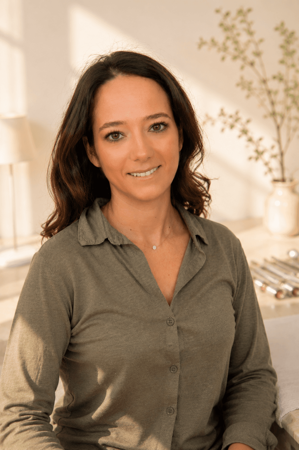 Portrait d'une femme souriante aux cheveux bruns ondulés vêtue d'une chemise boutonnée vert olive.